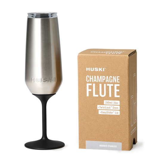 Silver champagne flute with black stem next to its packaging on a white background