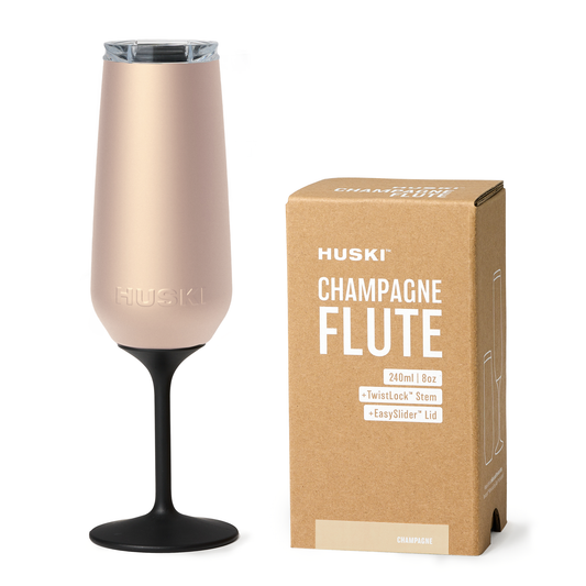 Rose gold champagne flute with black stem next to its packaging box on a white background