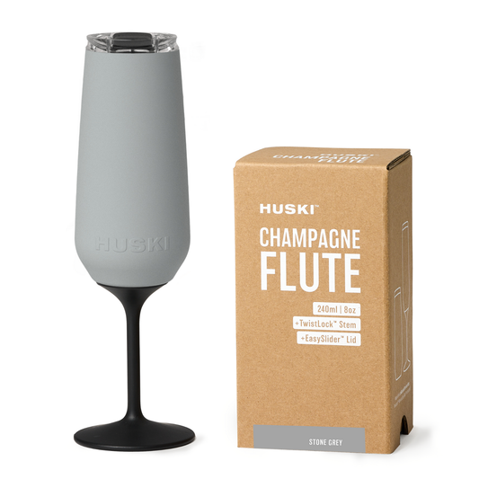 Gray champagne flute with black stem and Huski branding next to its packaging on a white background