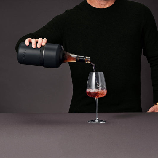 Person pouring red wine from a black container into a glass against a dark background
